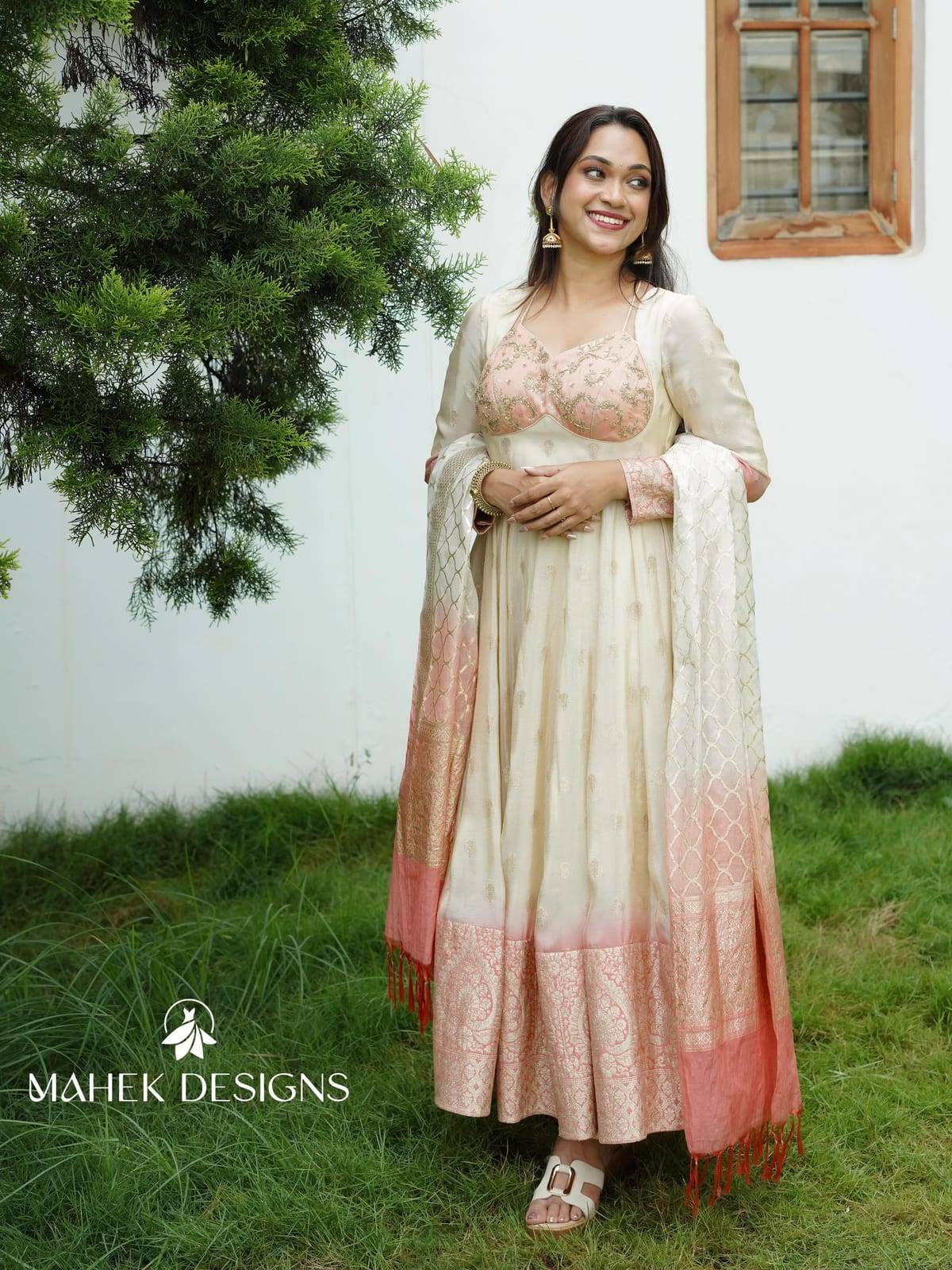 A graceful fusion of traditional elegance and contemporary charm, this ensemble features a soft ivory Anarkali crafted in a rich, flowing fa